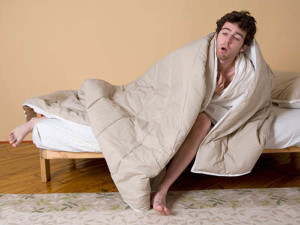 Young man wrapped in blanket on edge of bed
