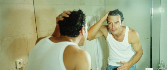 Man looking at reflection in bathroom mirror, wet face and hair